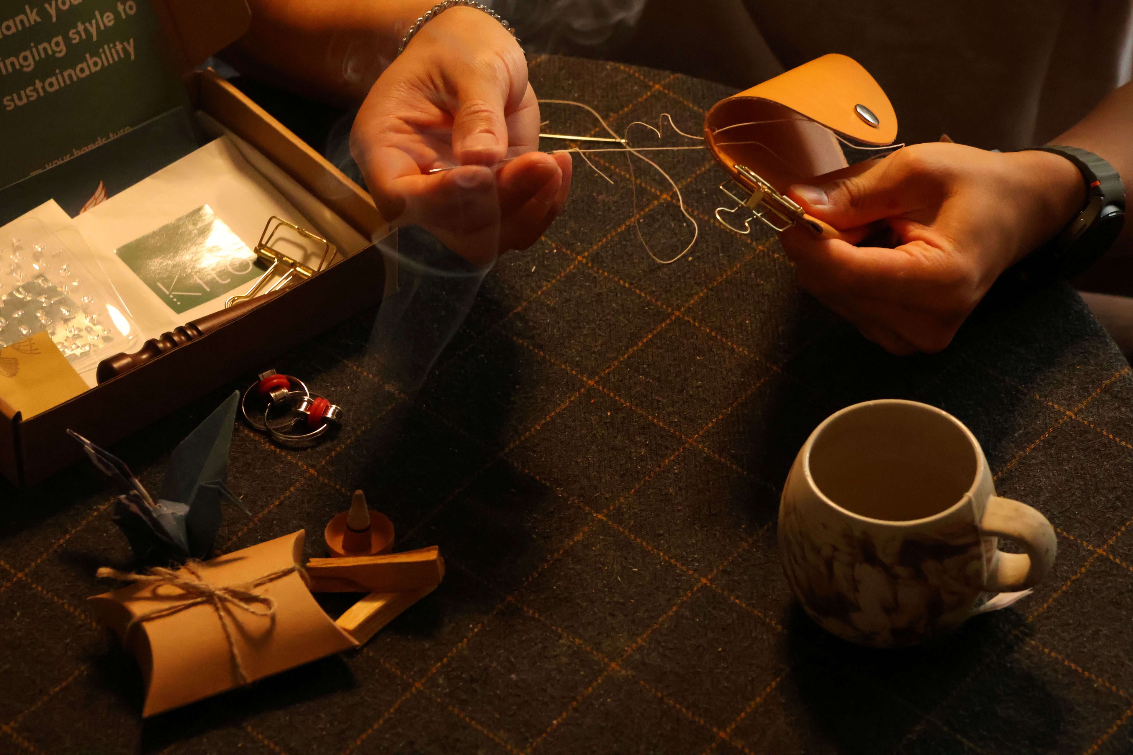 Person threading a needle with a small box and mug on a textured surface