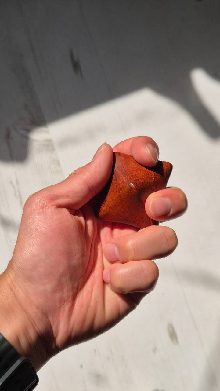 Hand holding a Vietnam rosewood massage ball against a neutral background