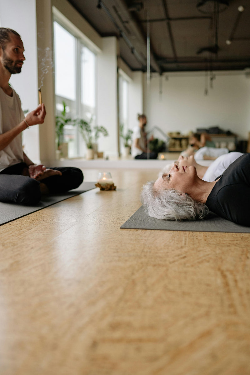 Two people practicing yoga in a studio with large windows and plants.